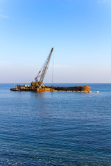 Fototapeta premium The Elevating Crane Unloads Stones from the Barge at Sea.