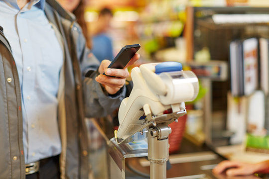 Mann zahlt mit Smartphone an Kasse im Supermarkt