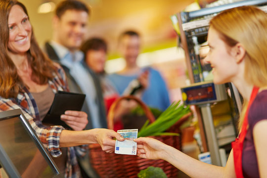 Frau zahlt mit Euroschein an Kasse im Supermarkt