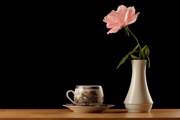 Pink rose in white vase and coffe cup isolated black bacground