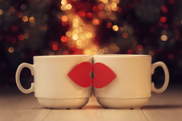 Two cups with red hearts on wooden table against defocused light