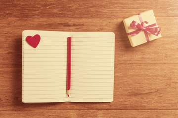 Open notebooks with red hearts and gift box on wooden background