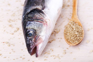 Fresh fish and salt in spoon on wooden background