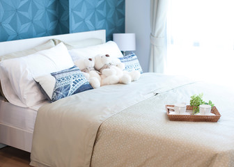 Decorative tray with teddy bear, tea set and flower on the bed