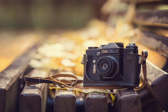 Vintage camera on wooden bench in autumn park. Instagram style t