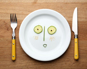 Vegetable face on plate with knife and fork on wooden table