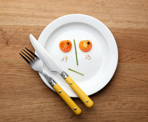 Vegetable face on plate with knife and fork on wooden table