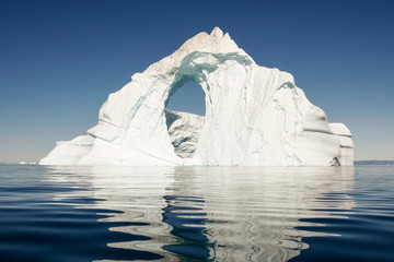 A lone iceberg floats in a still, deep blue sea.