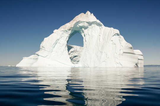 A lone iceberg floats in a still, deep blue sea.