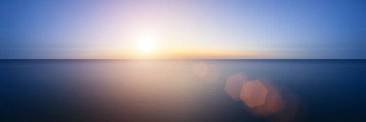 Conceptual image of sunset with added lens flare over still wate