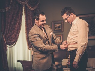 Tailor measuring client for custom made suit tailoring