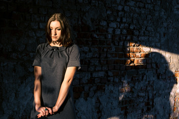 Beautiful young woman stands near the old brick wall