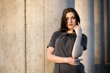 Young woman in a gray stands near the concrete pillar