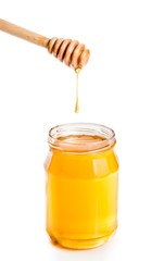 honey jar on white background with wooden dipper on top and drop