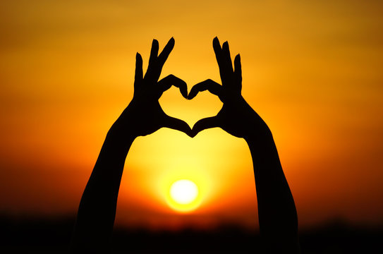hand forming a heart shape with sunset silhouette