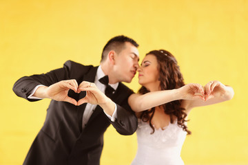 Bride and groom kissing against yellow wall