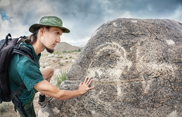Man touching petroglyph with goat - obrazy, fototapety, plakaty