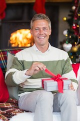 Obraz na płótnie Canvas Smiling man opening a gift on christmas day