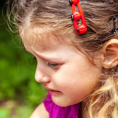 Cute little girl crying on the background of green grass. © trotzolga