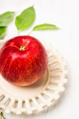 Red apple in  vintage plate with leaves on white wooden