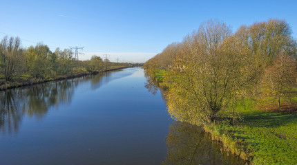 Trees along a canal under sunny sky in autumn