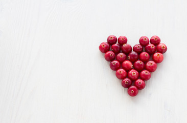Cranberries in the shape of a heart on a white wooden background