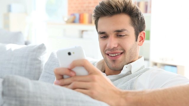 Casual guy using smartphone, relaxing in couch