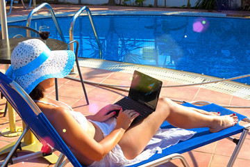 Young Woman sunbathing on deckchair with laptop