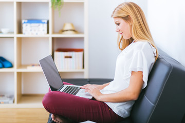 Smiling young woman looking on your laptop sitting on sofa at ho - 73673874