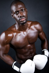 Young athletic boxer wearing gloves in black background.