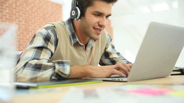 Young office worker using headphones in front of laptop