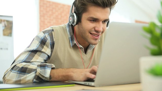Young office worker using headphones in front of laptop