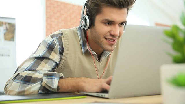 Young office worker using headphones in front of laptop