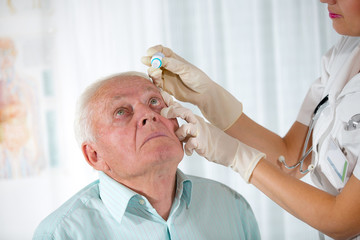 Doctor putting drops into a senior man's eyes