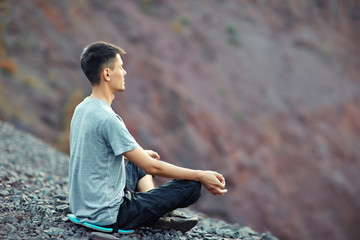 Naklejka na ściany i meble Young man relaxing on rocky cliff