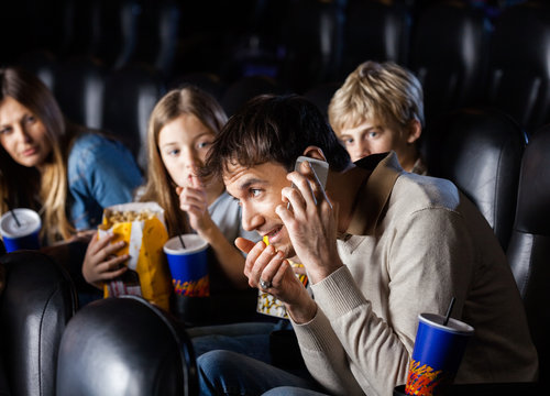 Angry Family Looking At Man Using Mobilephone In Theater