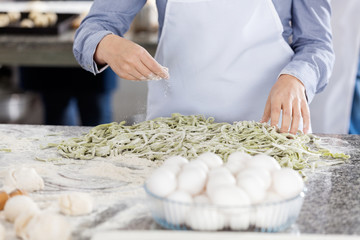 Chef Sprinkling Flour On Spaghetti Pasta At Counter In Kitchen