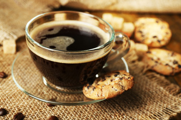 Glass cup of coffee and tasty cookie on wooden background