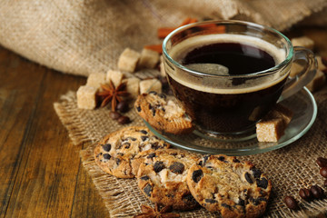 Glass cup of coffee and tasty cookie on wooden background