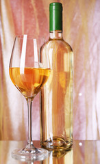 Wine bottle and wineglass with white wine on bright background
