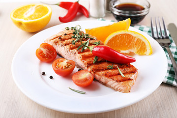 Grilled salmon and vegetables on plate on wooden background