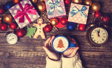 Female holding cup of coffee with cream christmas tree on a tabl