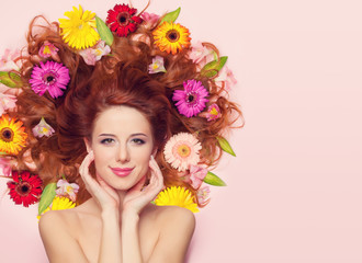 Obraz na płótnie Canvas Beautiful redhead girl with flowers on pink background