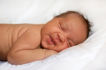 newborn baby girl sleeping. Black baby on white bed.
