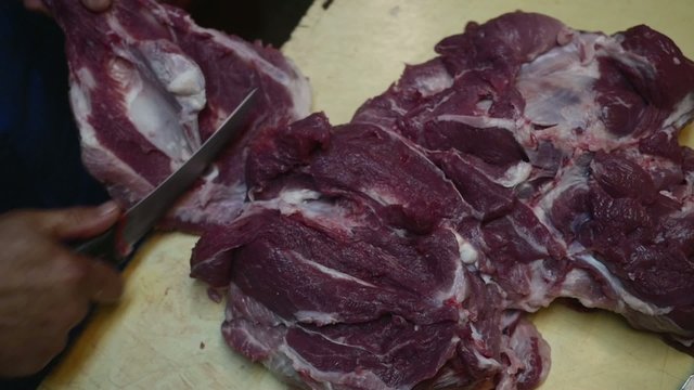 Old butcher cutting meat with knife in slow motion