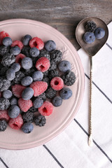 Iced berries on plate, on color wooden background