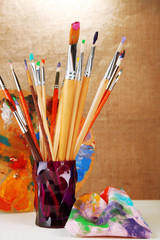 Fototapeta premium Paint brushes with paints and palette on beige background