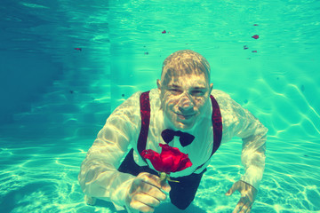 Obraz na płótnie Canvas Groom offering a red rose pool water dive underwater