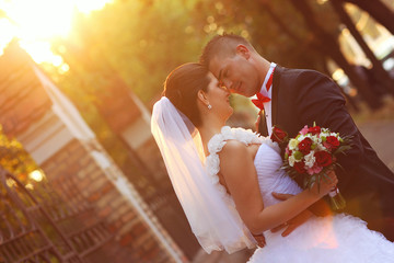 bride and groom kissing at sunset with a flower bouquet