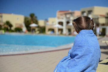 Little girl in a blue towel resting near the pool after swimming